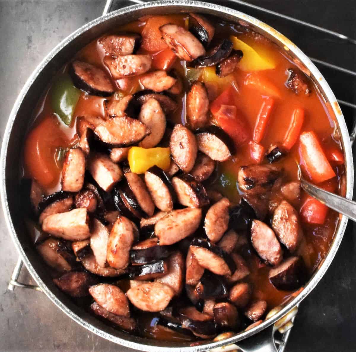 Pepper stew with chopped browned sausage in pot.