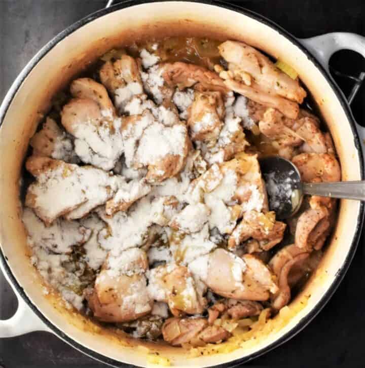 Chicken pieces with flour in pot with spoon.