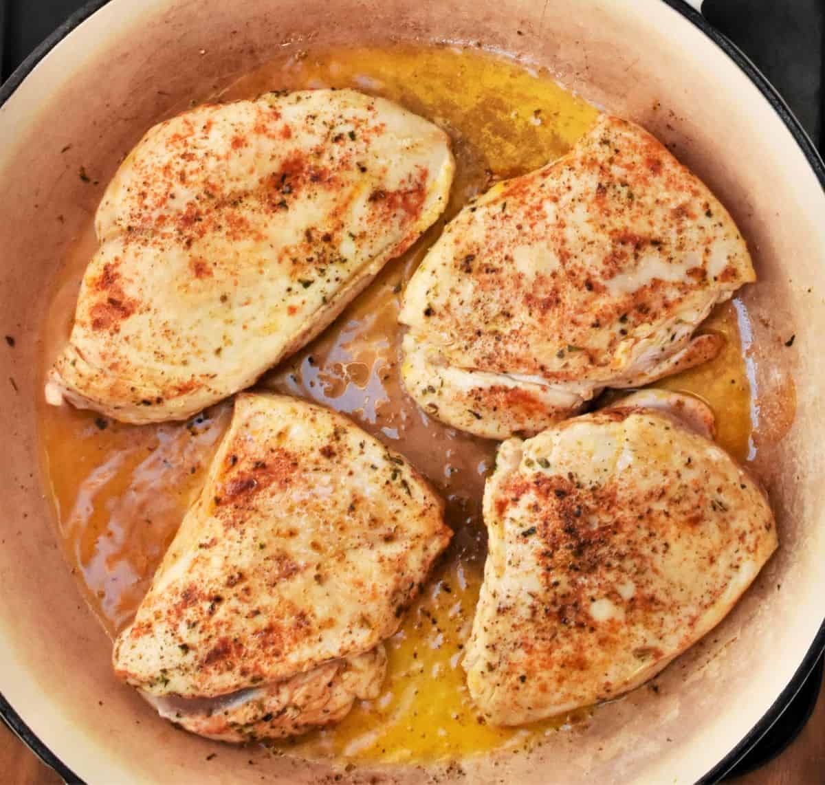 Top down view of 4 seared chicken breasts in oil in large pan.