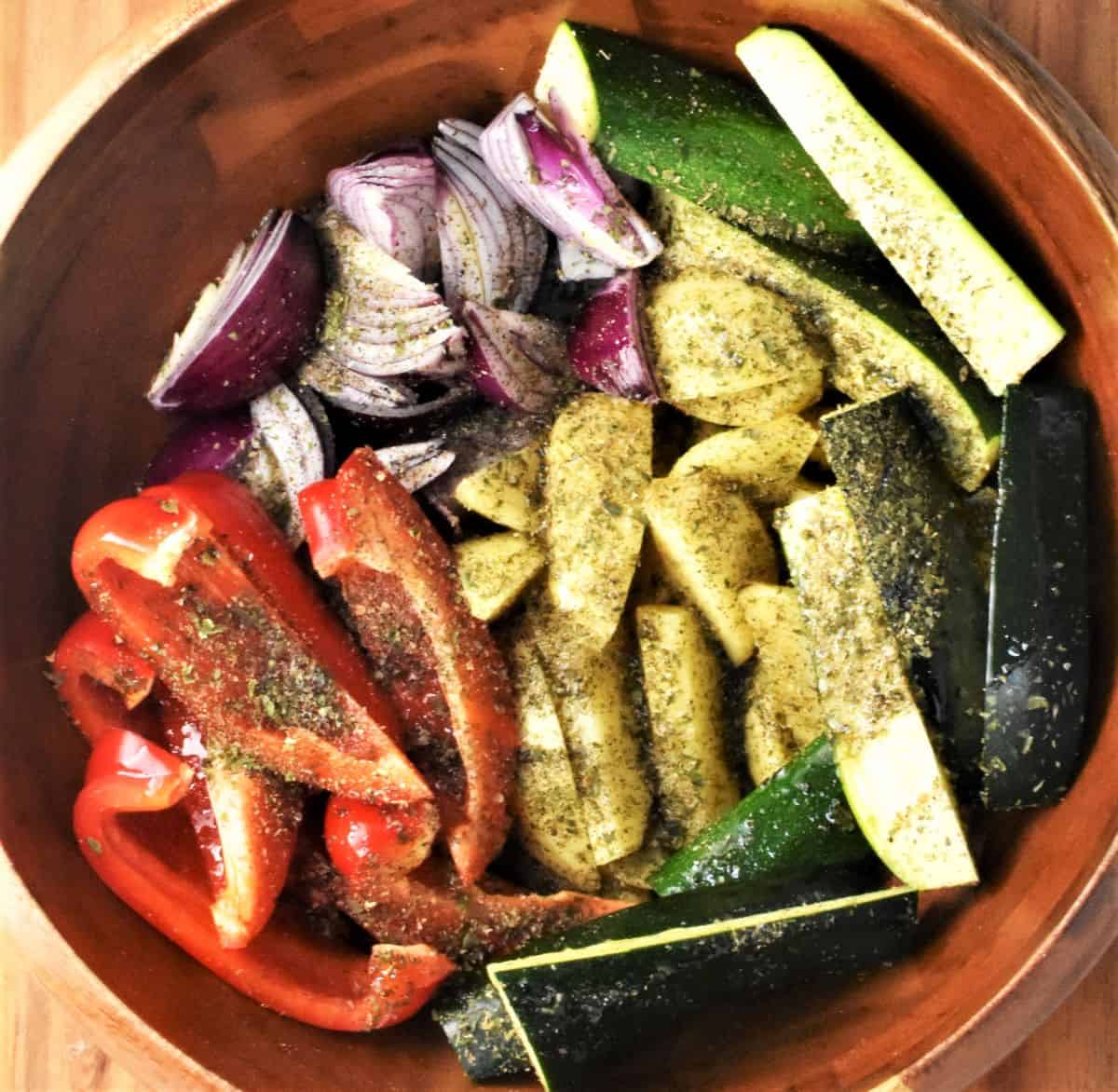 Pieces of vegetables coated in herbs in brown bowl.