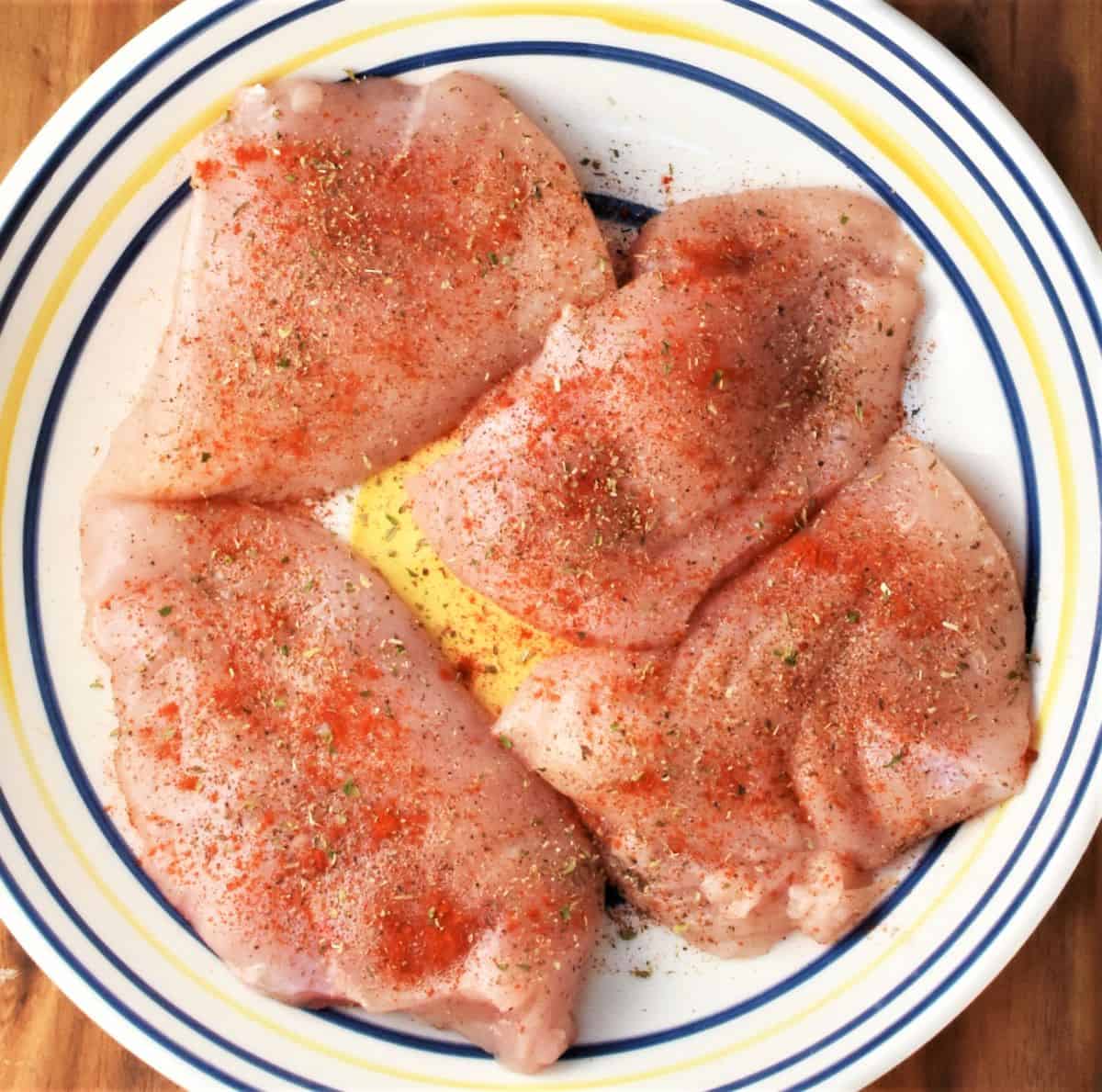 4 skinless chicken breasts with seasoning in large bowl.