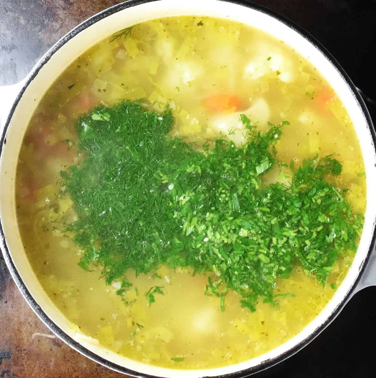 Soup with chopped fresh herbs on top in white pot.
