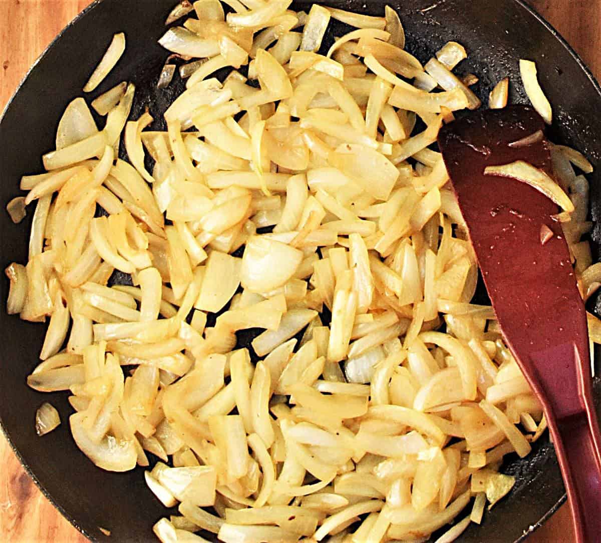 Slices of onion in large skillet with red spatula.