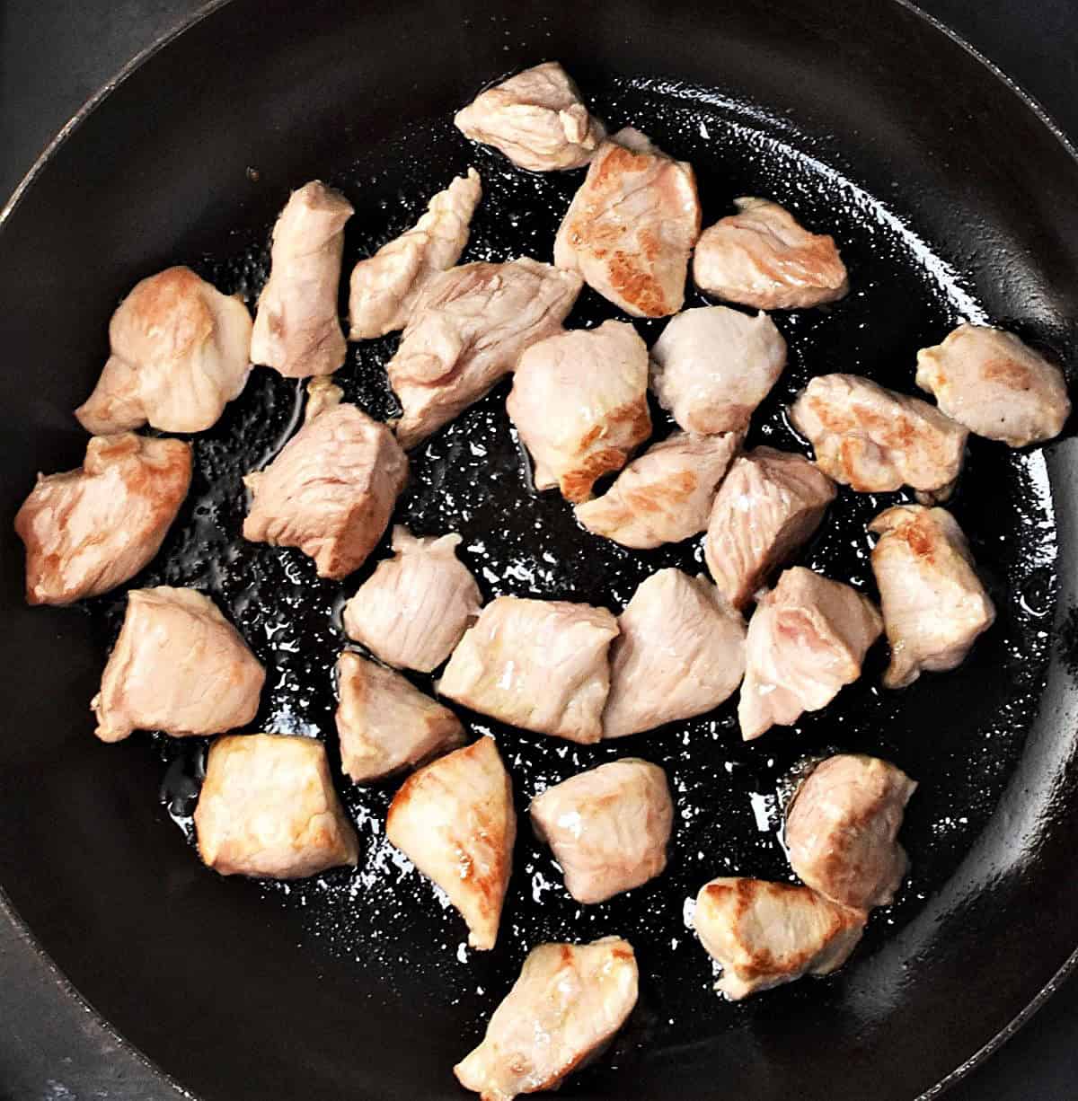 Chunks of browned pork meat in large skillet pan.