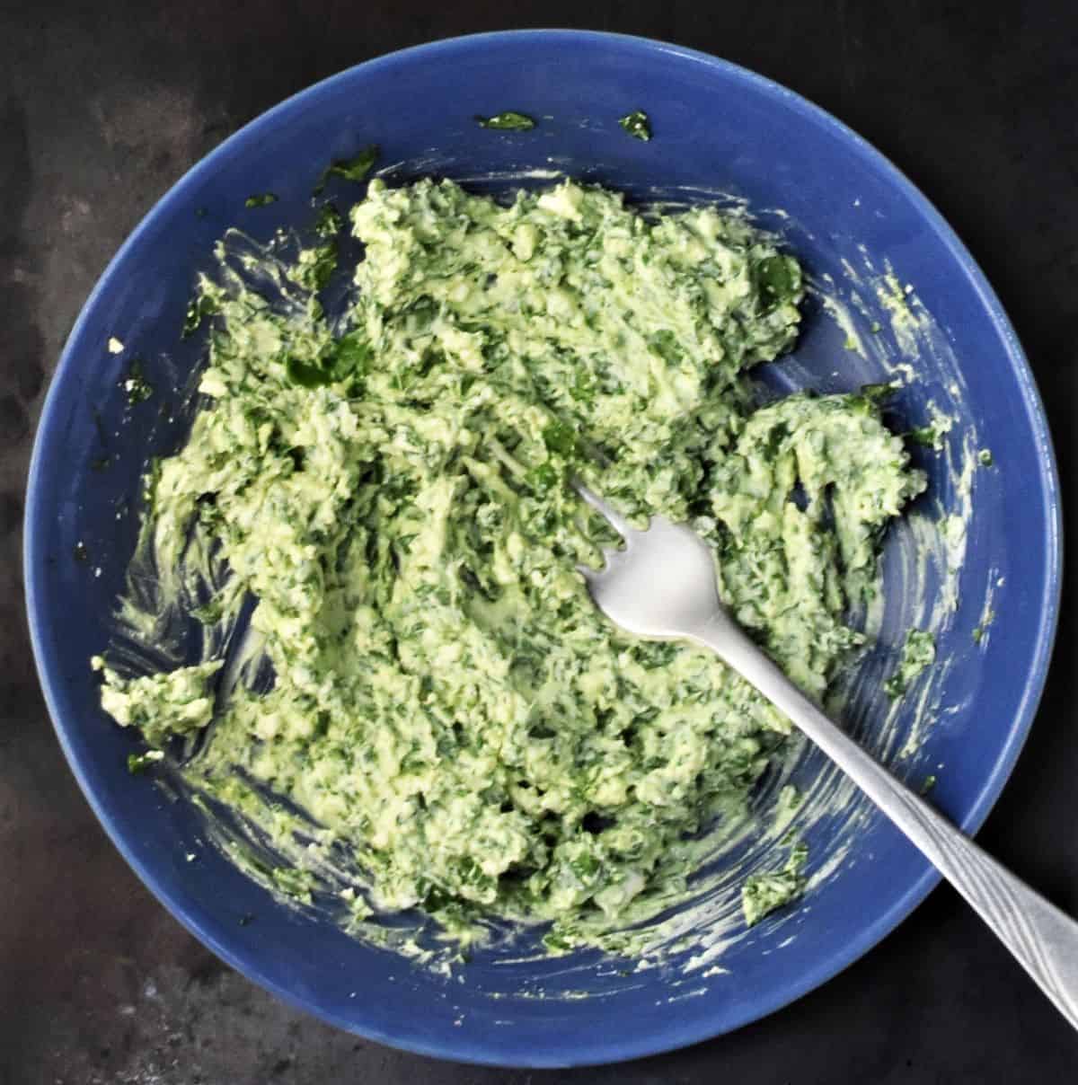 Creamy spinach mixture in blue bowl with fork.