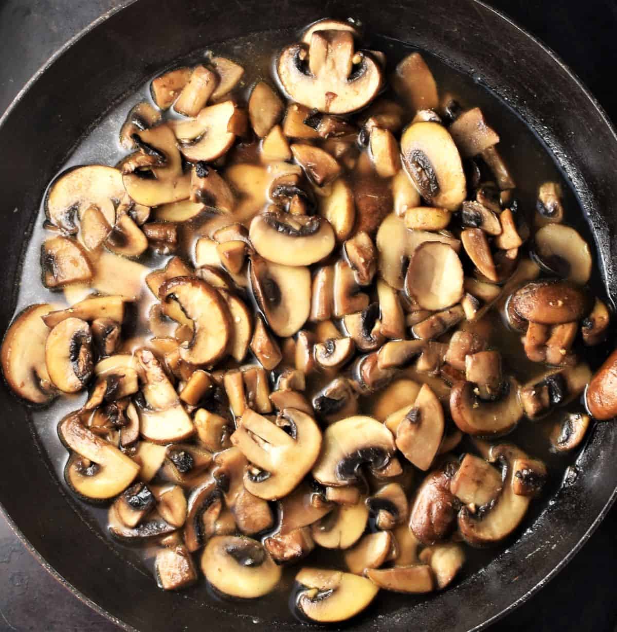 Cooked mushrooms with water in large shallow pan.