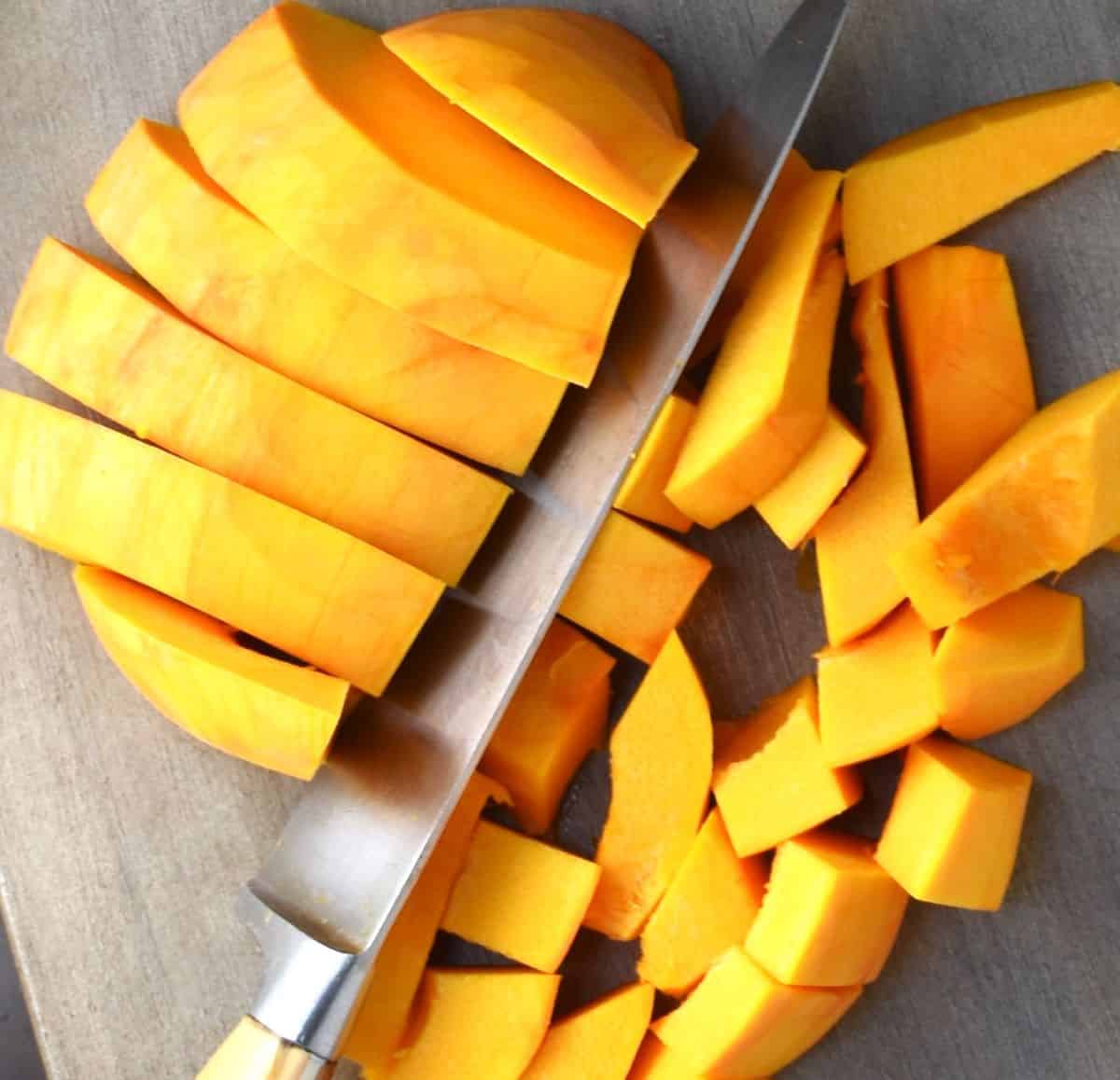 Chopping peeled pumpkin on top of cutting board.