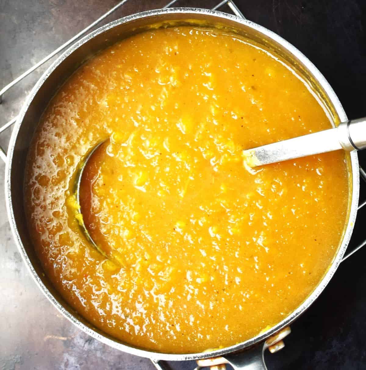 Top down view of creamy soup in pot with ladle.