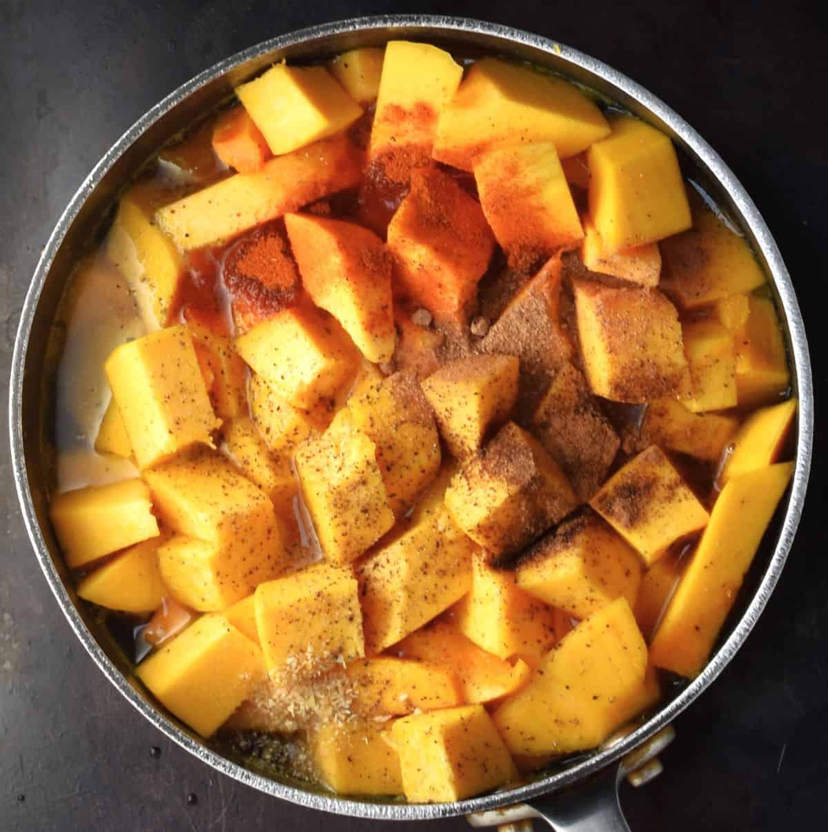 Cubed pumpkin with spices and stock in pot.