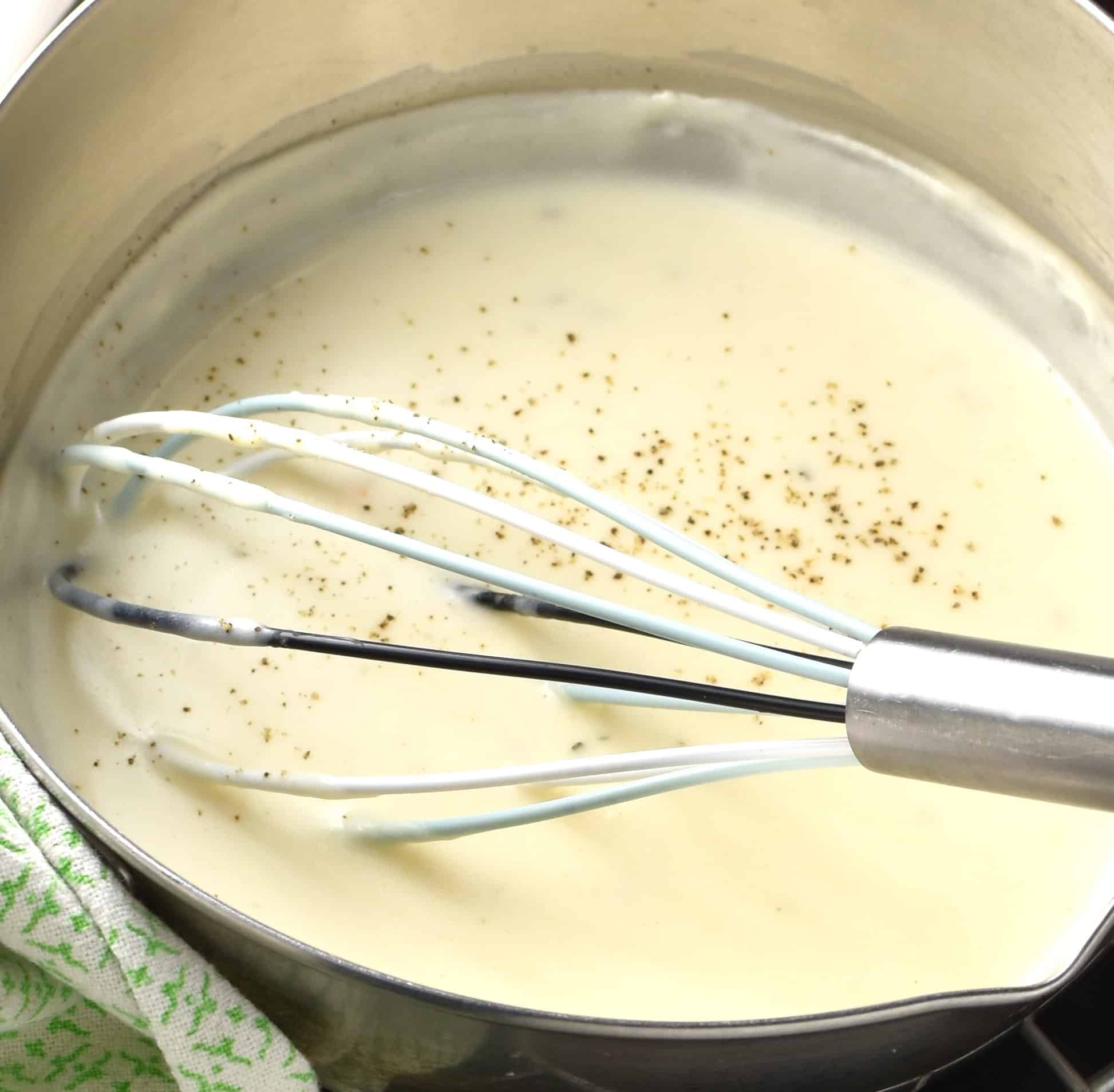 Close-up side view of creamy sauce with sour cream and whisk in saucepan.