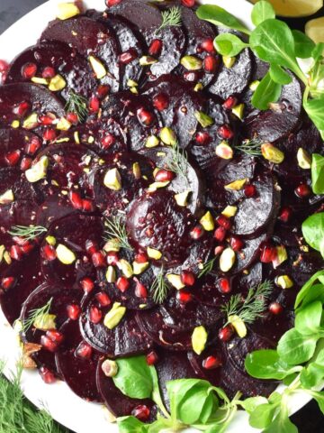 Top down view of beet carpaccio with pomegranate seeds on white plate.