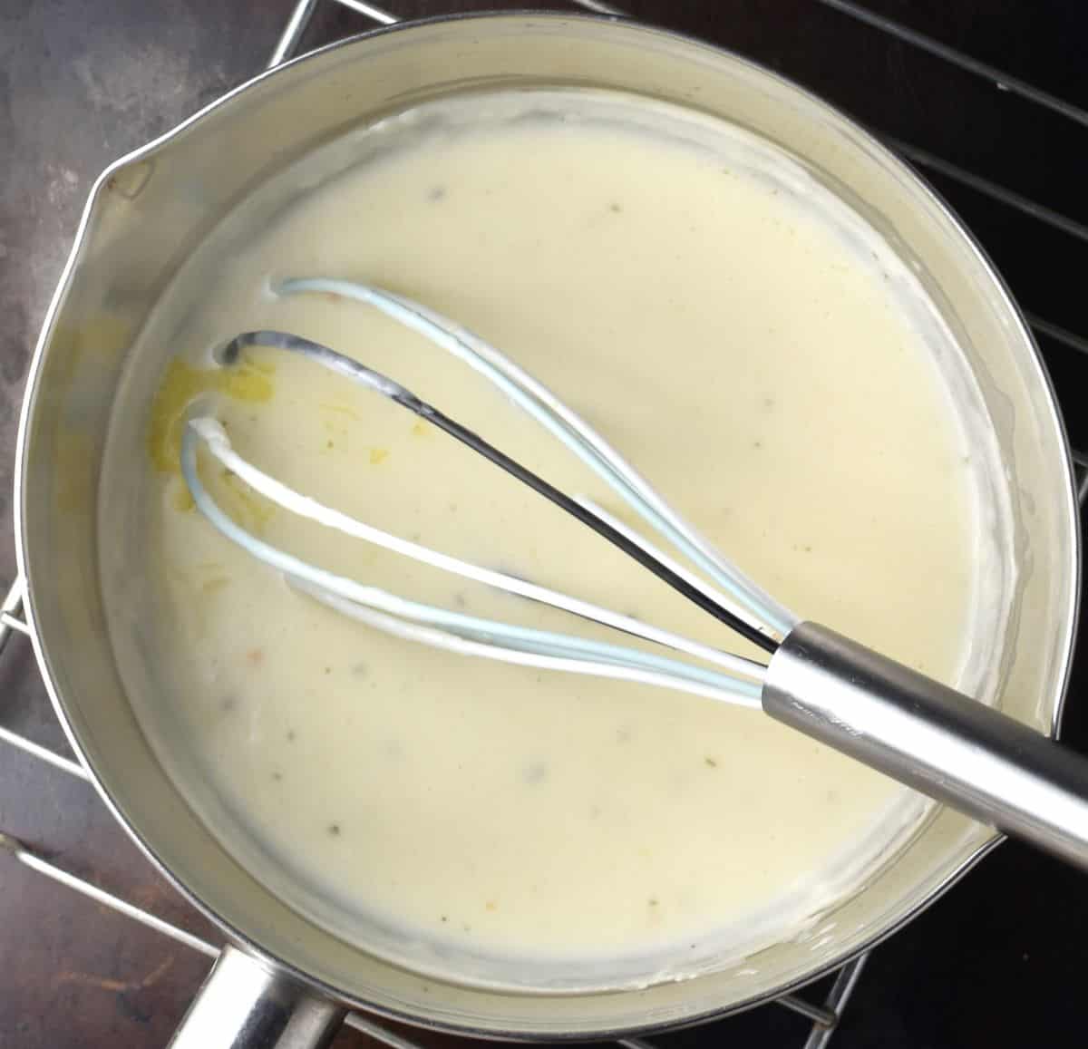 Creamy sauce in saucepan with whisk.