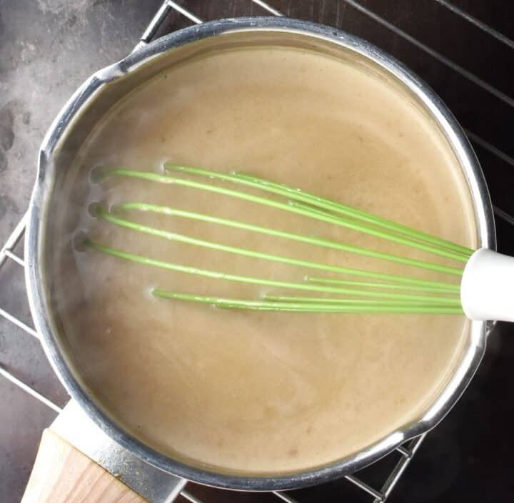 Creamy sauce with whisk in pot.