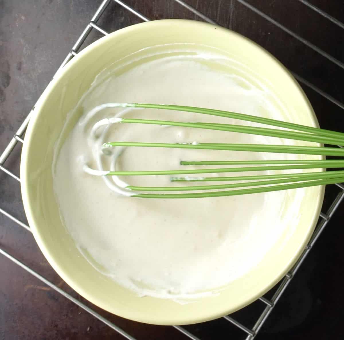 Creamy mixture with whisk in yellow bowl.