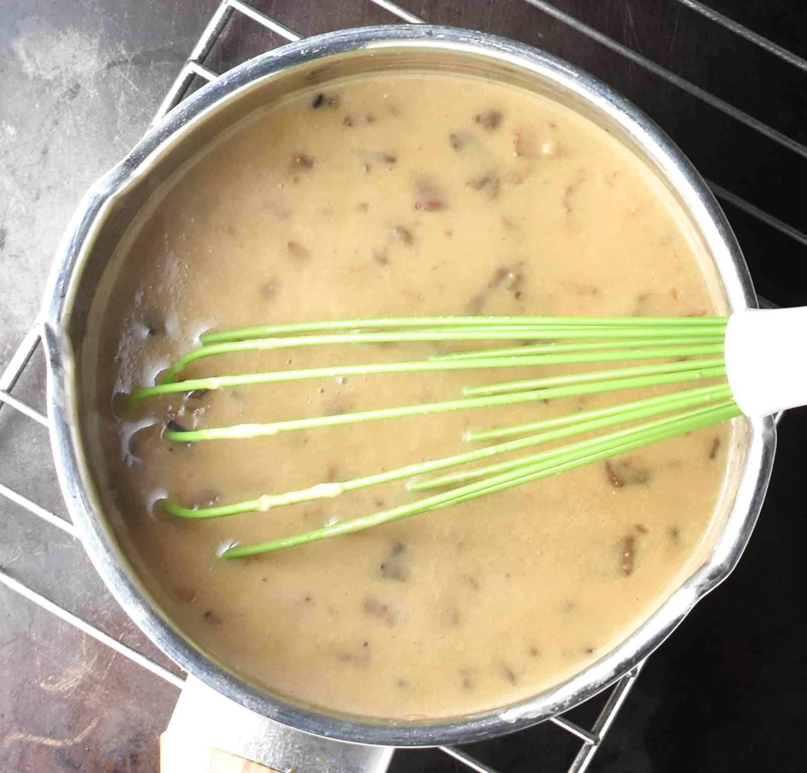 Creamy sauce with finely chopped wild mushrooms in pan with whisk.
