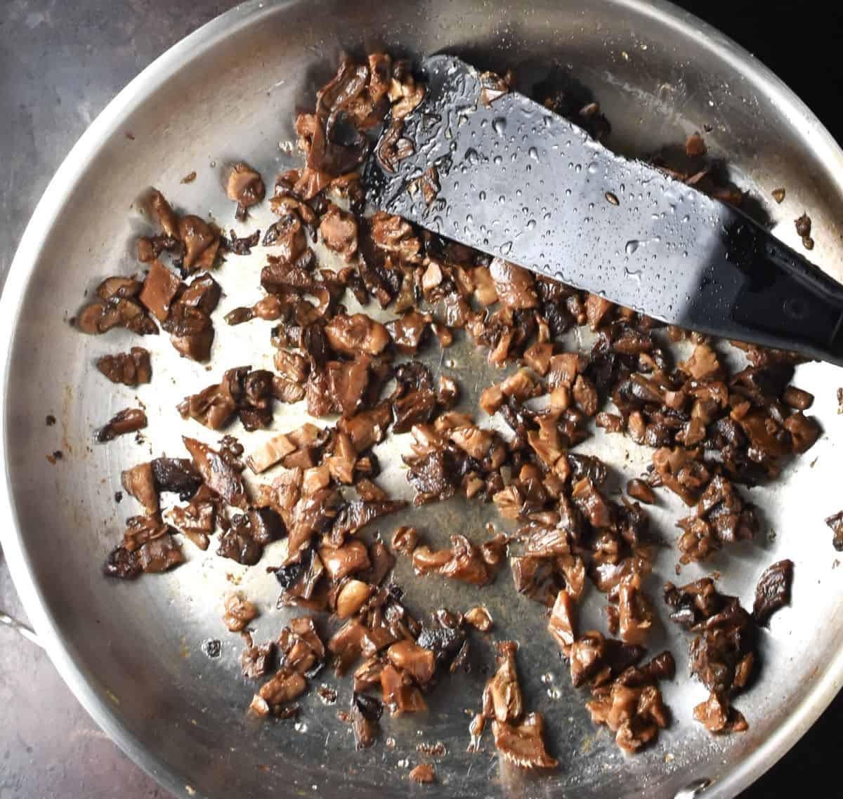 Finely chopped wild mushrooms in pan with black spatula.