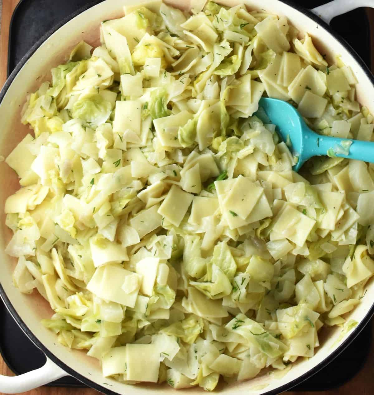 Top down view of pasta with cabbage in shallow pan with blue spoon.
