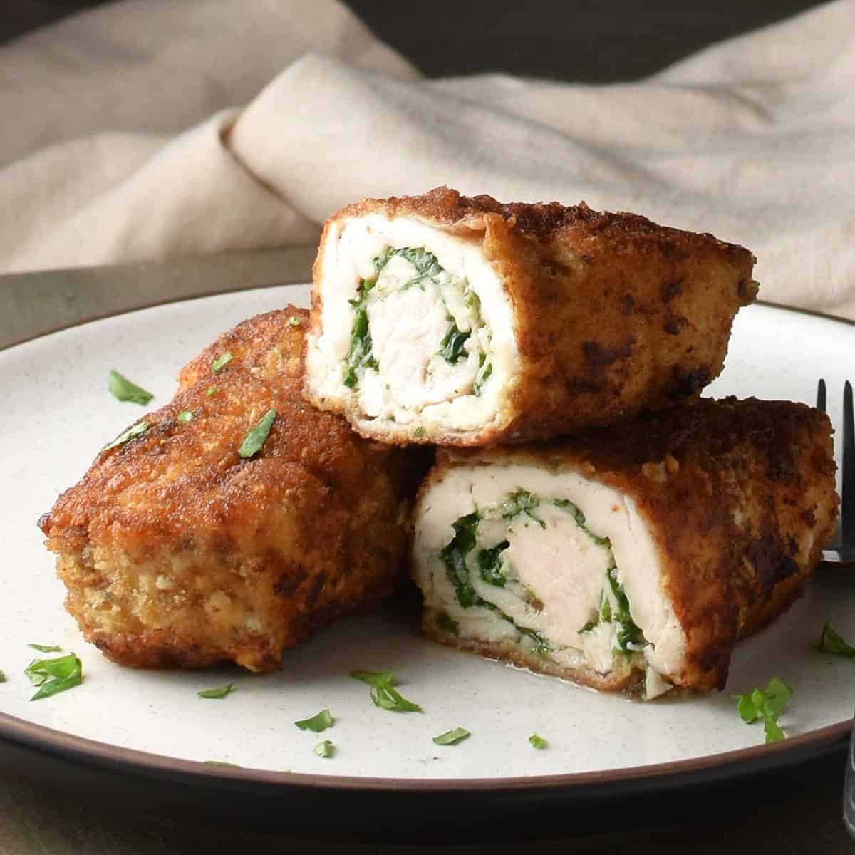 Side view of breaded halved chicken roll-ups on white plate.