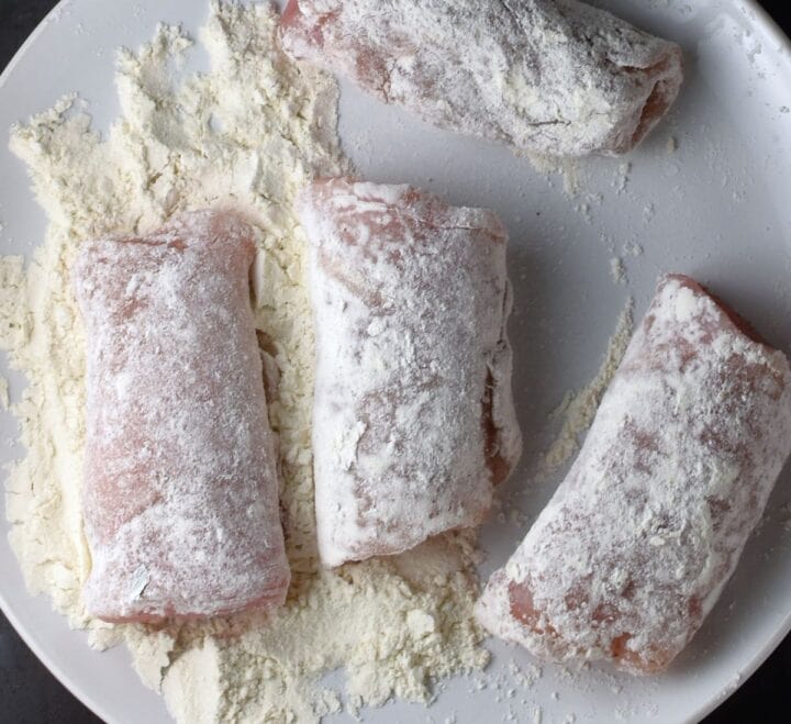 4 chicken roll-ups coated in flour on plate.