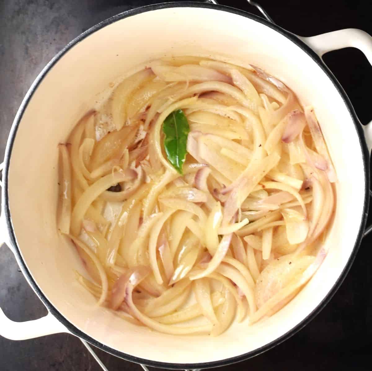 Sliced onion with bay leaf in white pot.