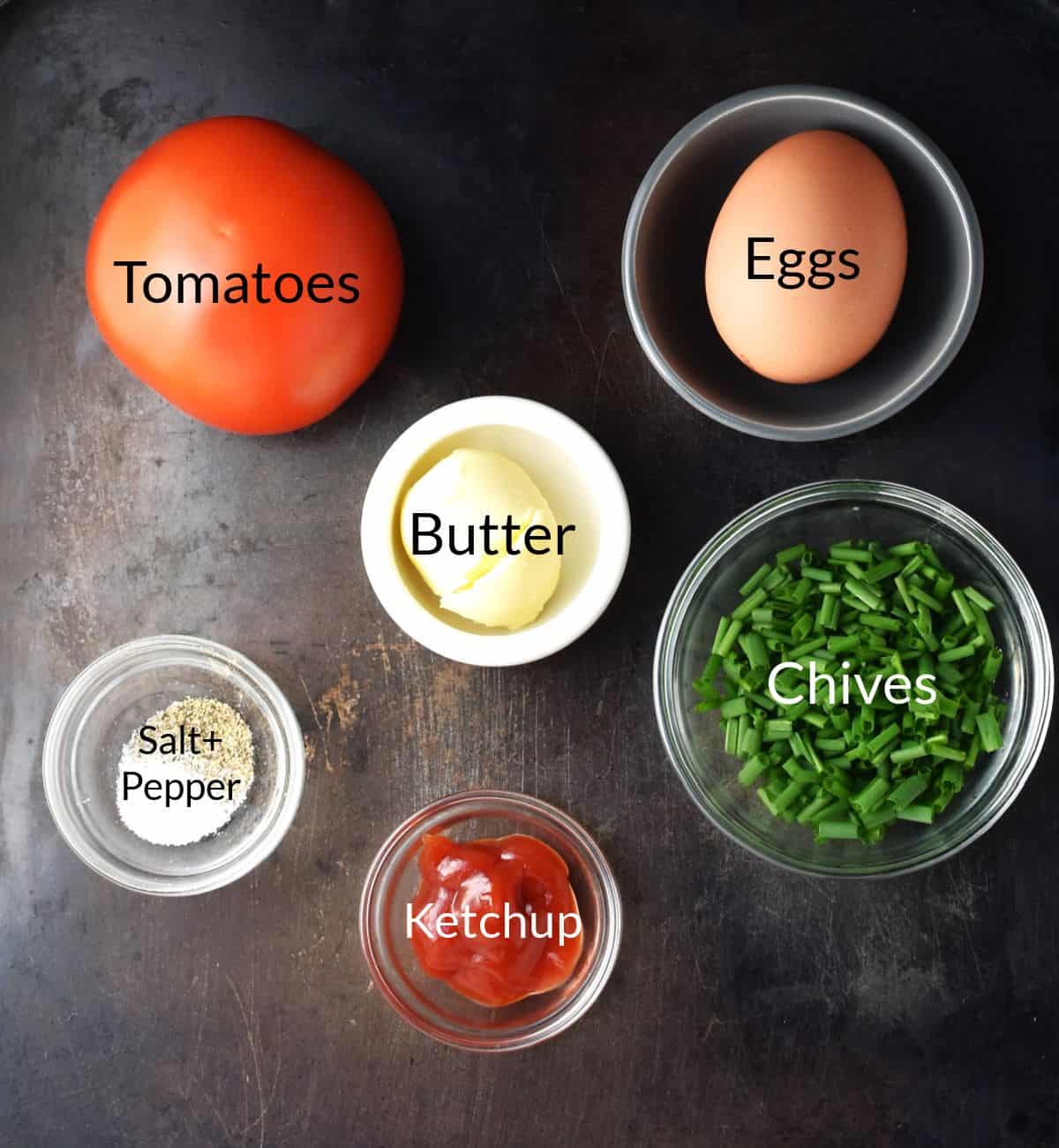 Top down view of ingredients for making scrambled eggs with tomato in individual dishes.