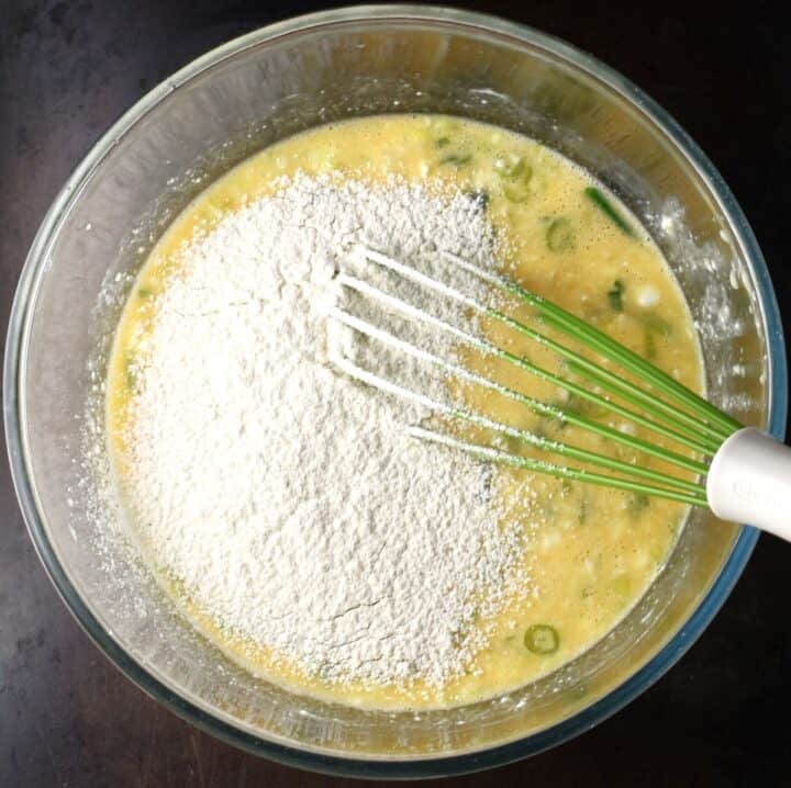 Adding flour to egg muffin batter in bowl with whisk.