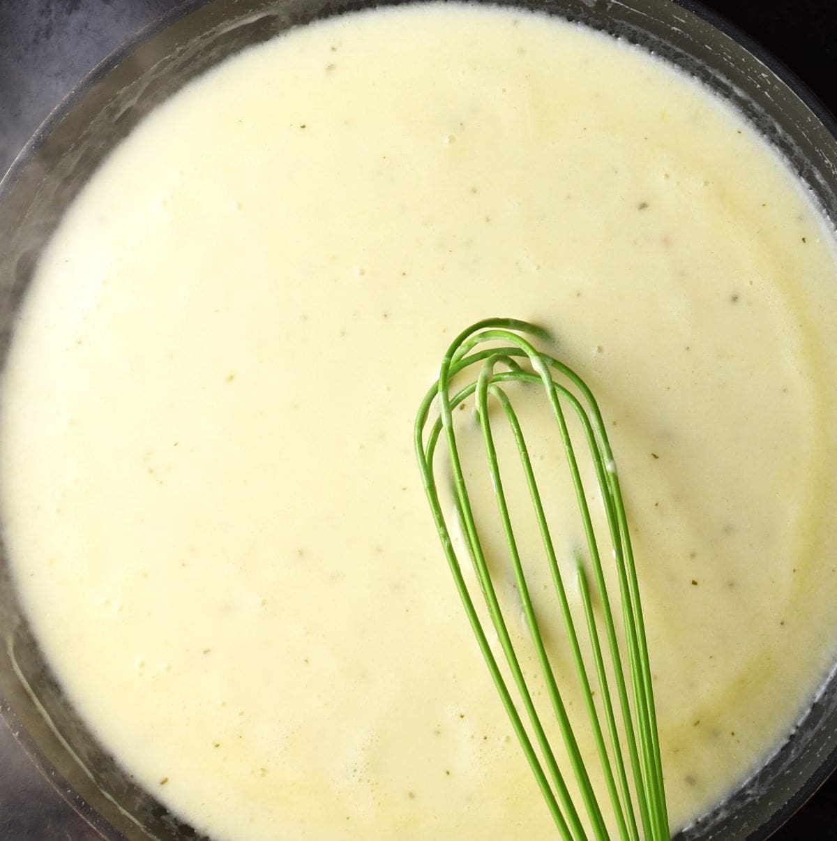 Creamy sauce in large pan with green whisk.