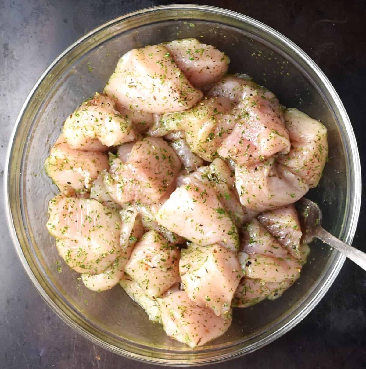 Diced chicken with herbs in glass bowl with fork.