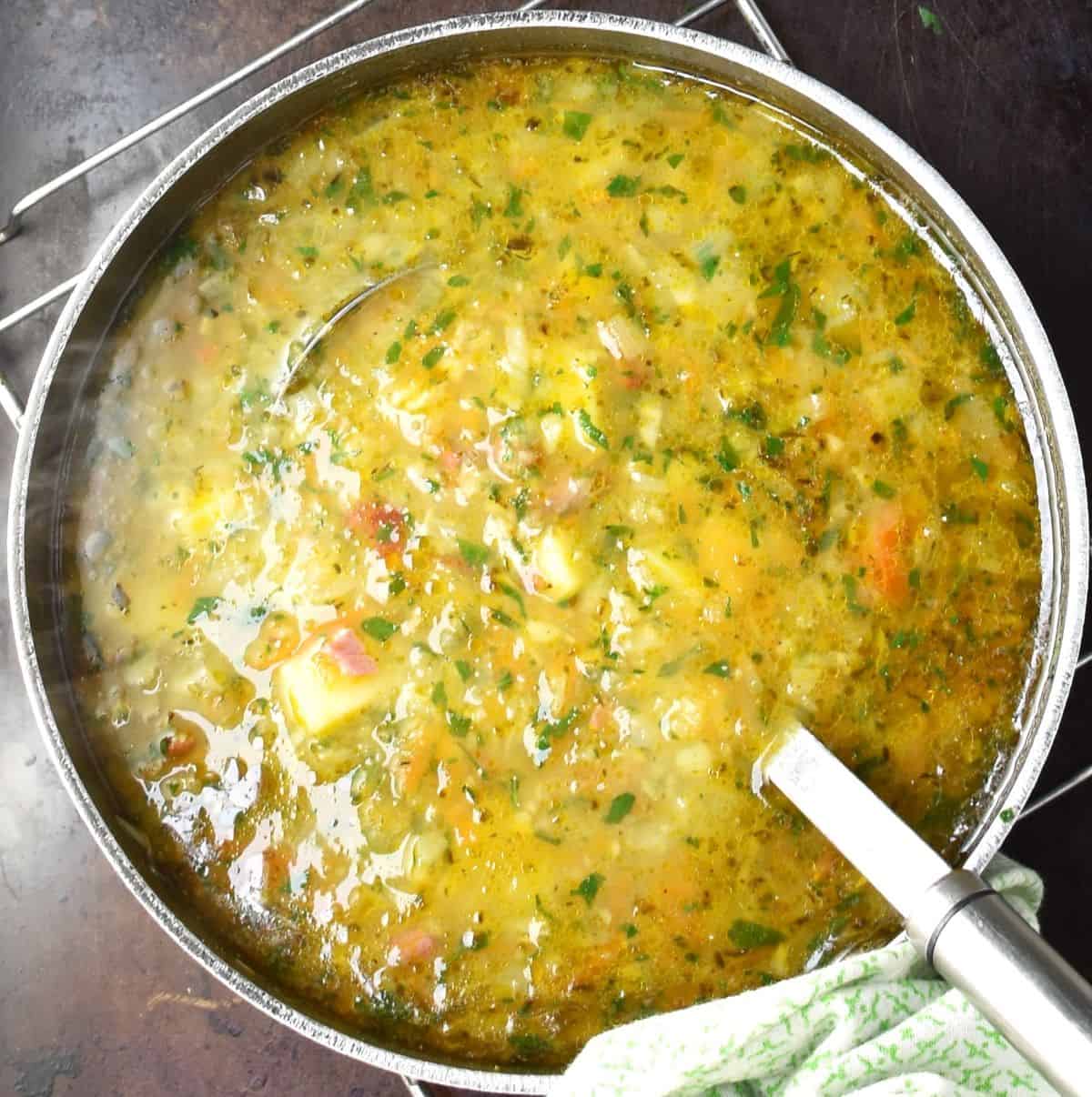 Top down view of chunky Polish potato soup in large pot with ladle.