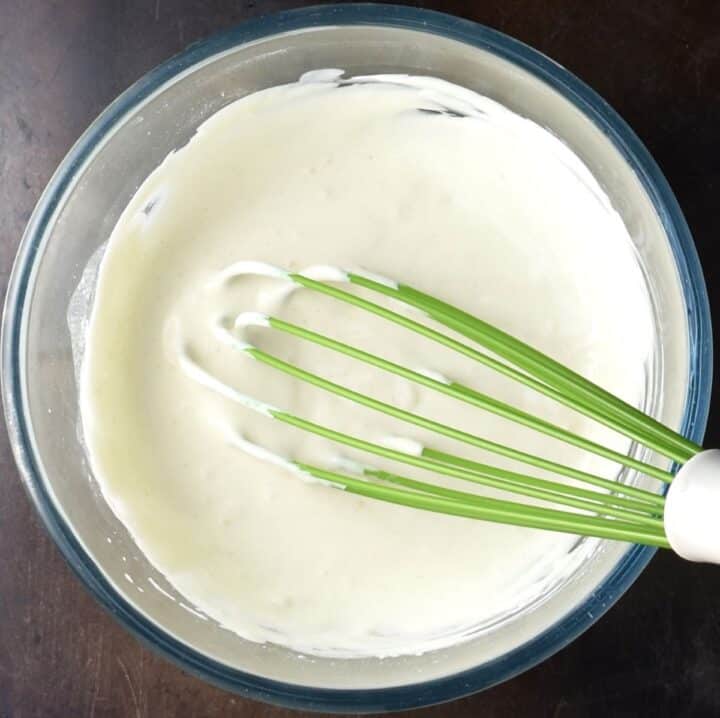 Creamy mixture in glass bowl with green whisk.