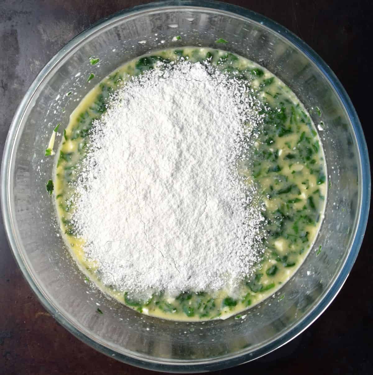 Spinach egg mixture with flour on top in glass bowl.