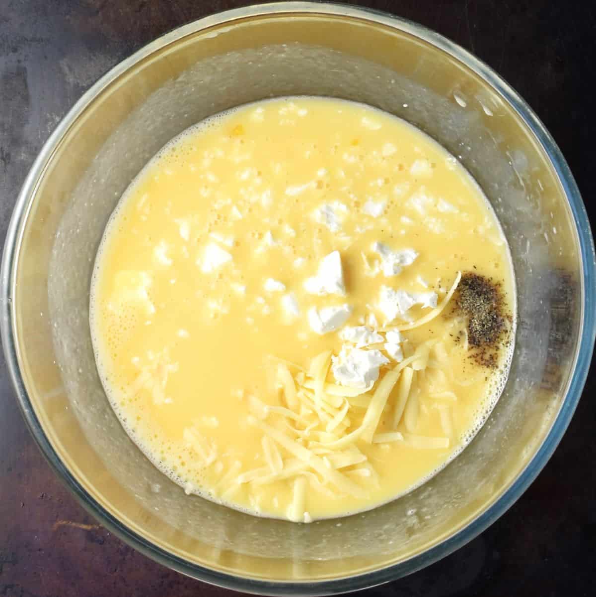 Top down view of egg mixture with grated cheese in glass bowl.