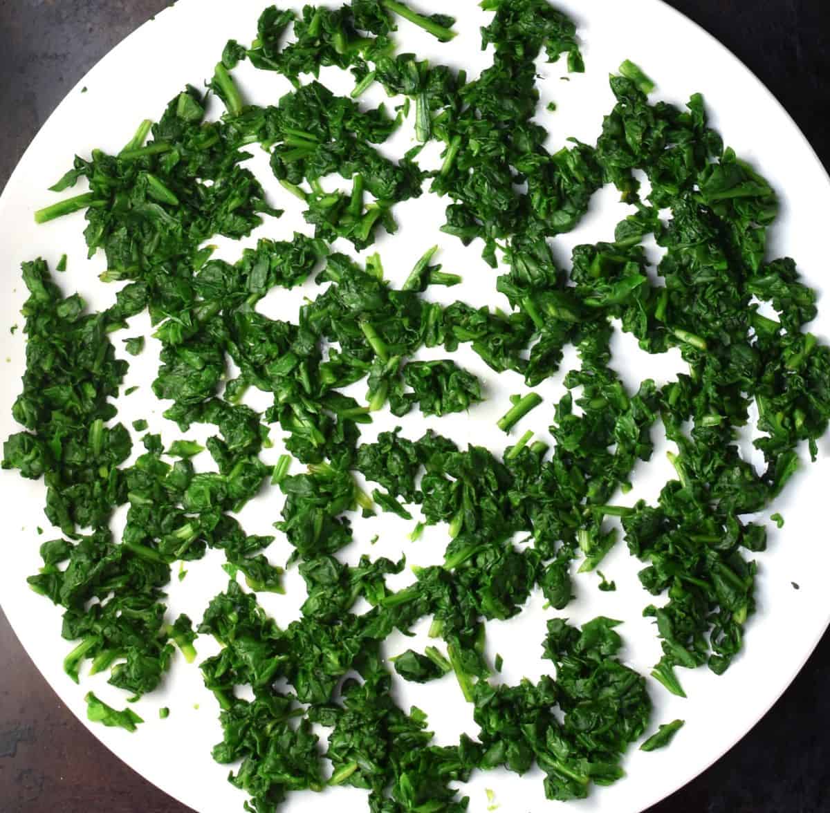 Top down view of wilted spinach spread over white plate.