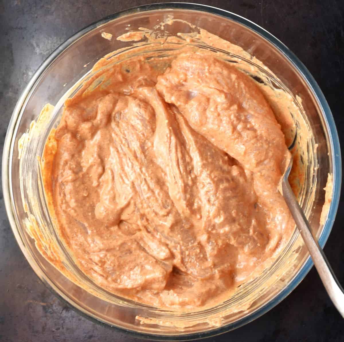 Top down view of chicken breast pieces in yogurt marinate in glass bowl with fork.