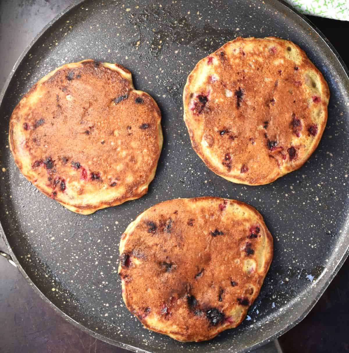Top down view of 3 raspberry pancakes in pan.