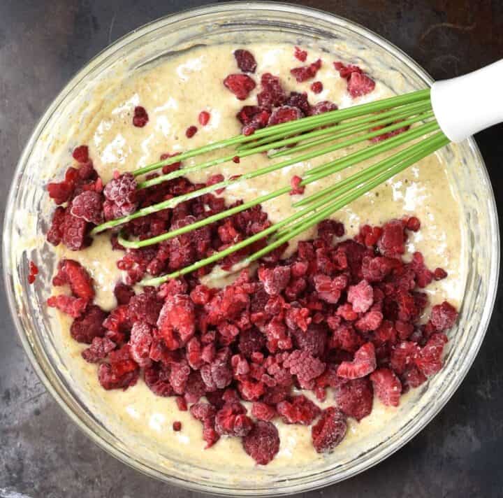Pancake batter with chopped raspberries on top in glass bowl with whisk.