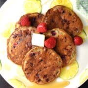 Top down view of 5 raspberry pancakes with fresh raspberries on top of yellow plate.
