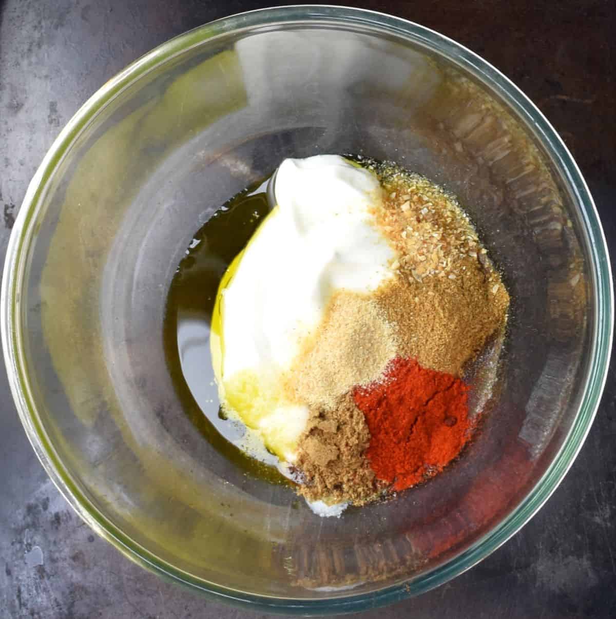 Yogurt marinade ingredients for chicken in large glass bowl.