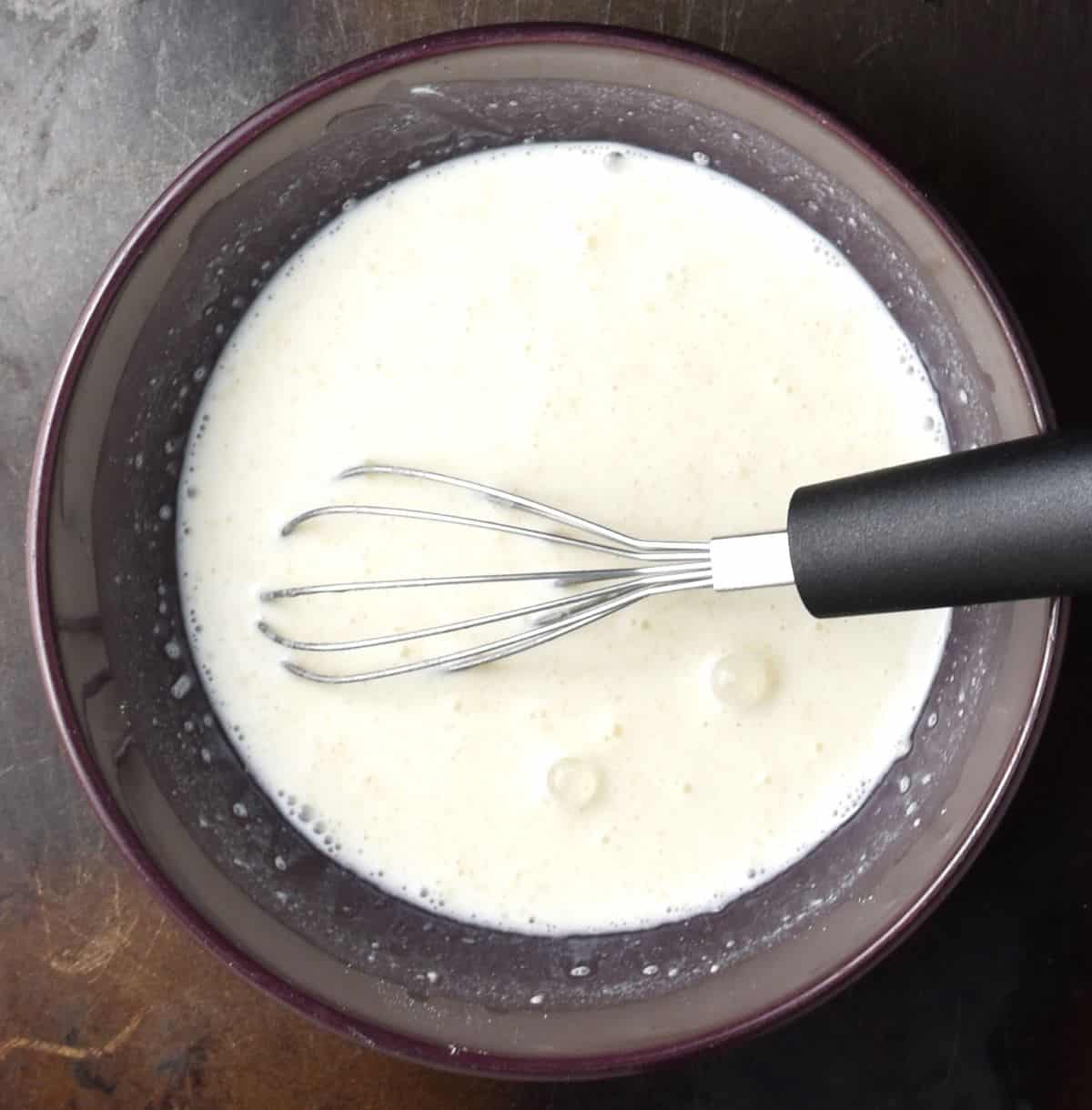 Creamy sauce base in purple bowl with whisk.