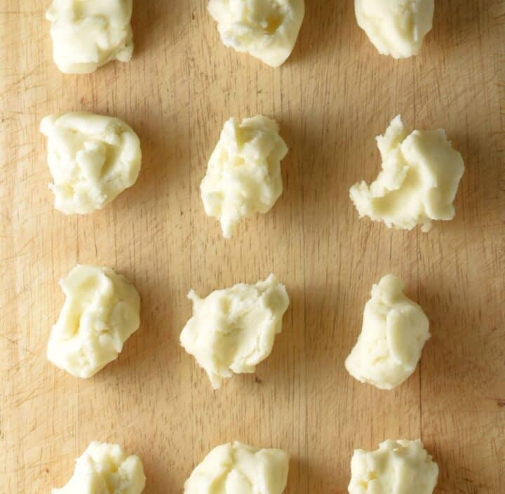 Dough pieces for kluski on top of wooden board.