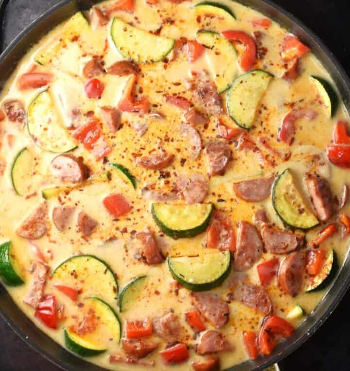 Top down view of kielbasa and vegetables in creamy sauce in pan.
