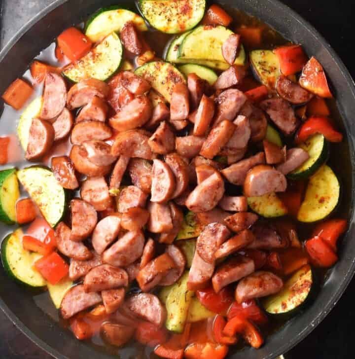 Kielbasa pieces with vegetables in large pan.