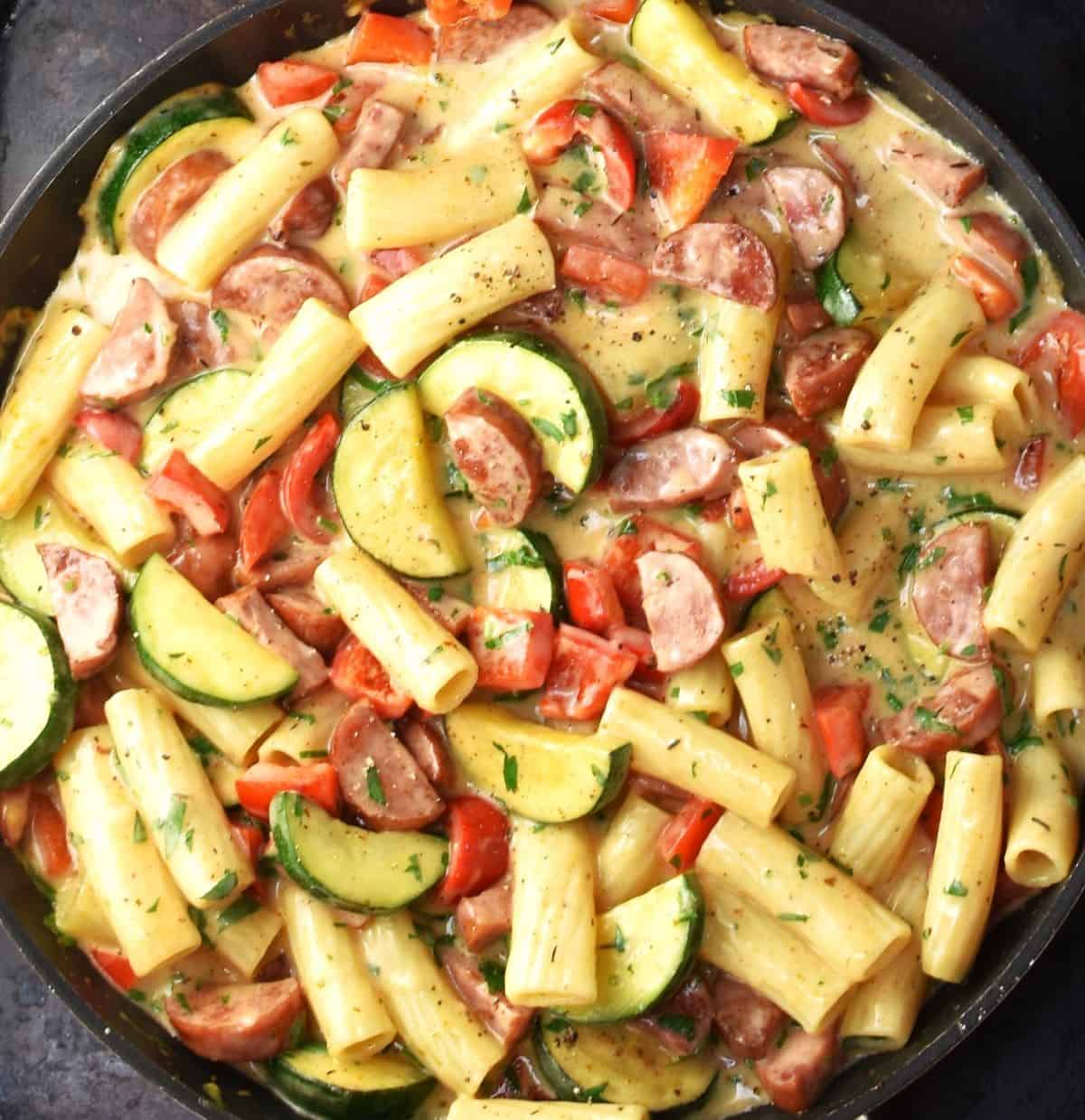 Pasta with kielbasa and vegetables in sauce in large pan.