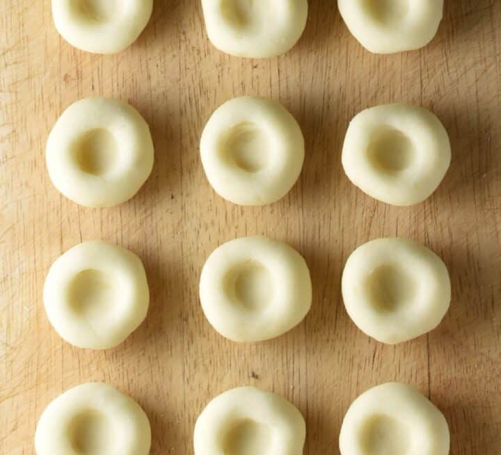 Raw Silesian kluski dumplings with dimple on top of board.