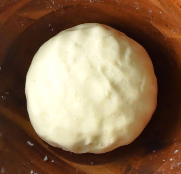 Top down view of round dough for kluski in wooden bowl.