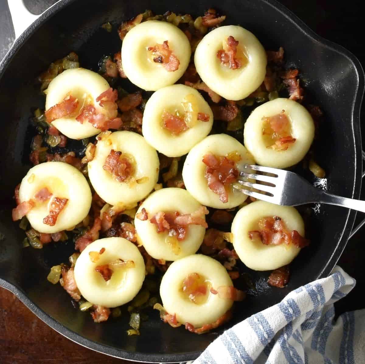 Top down view of silesian dumplings with bacon and onion in pan.