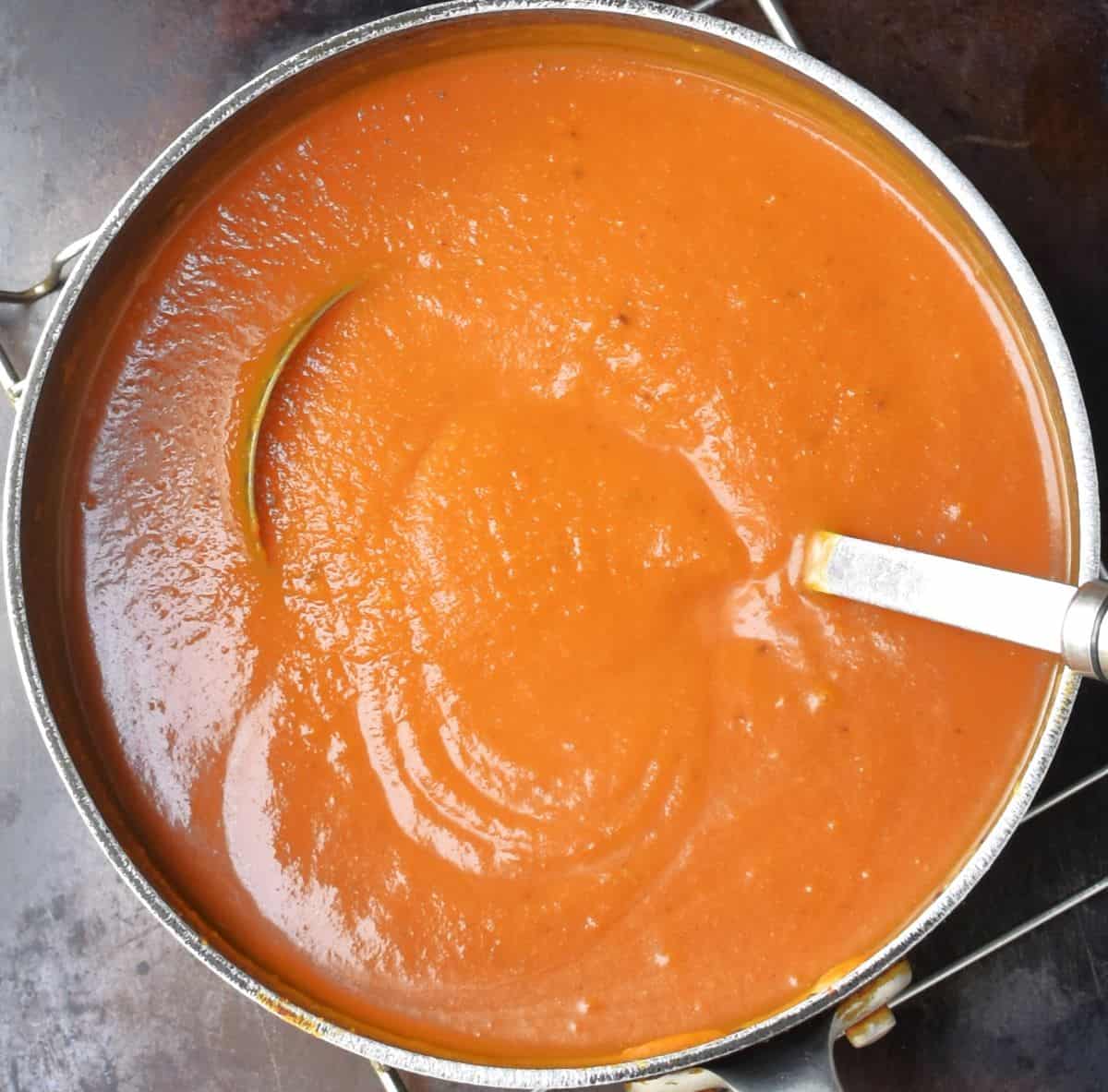 Top down view of creamy butternut and tomato soup in pot with ladle.