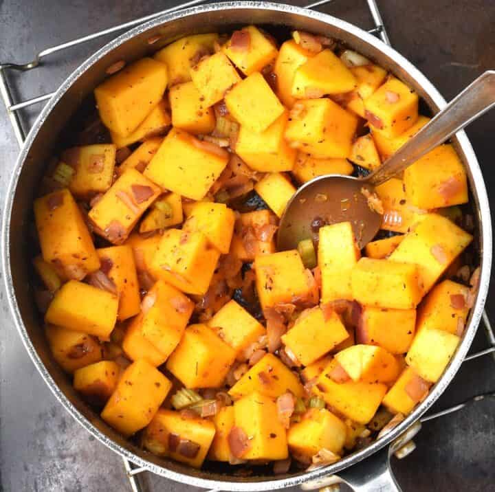 Cubed squash with onion in pot with spoon.