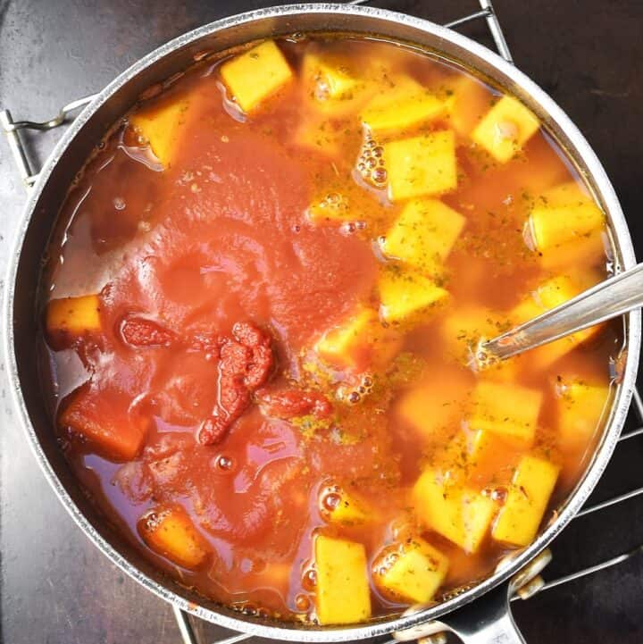 Passata and cubed butternut squash in pot with stock and spoon.