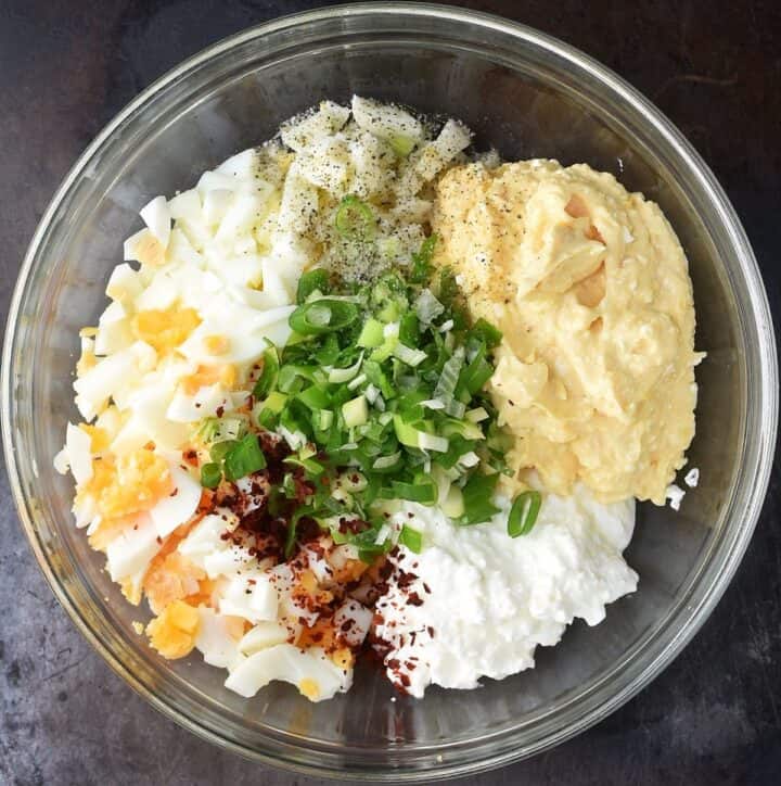 Top down view of cottage cheese and egg salad ingredients in glass bowl.